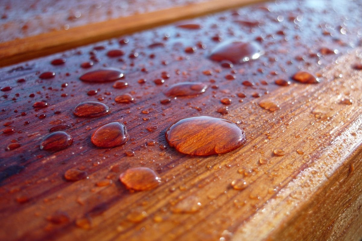 Cedar Deck Stain: Best Products and How to Apply 3 Close-up of oil-based stain being applied to cedar deck boards with proper back-brushing technique